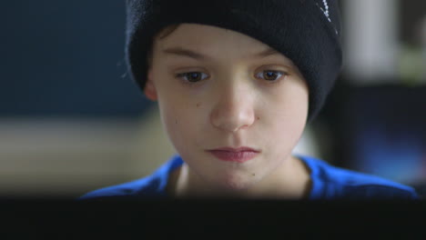 Young-boy-playing-games-on-his-laptop-concentrating-closeup-on-face