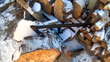 Axe-stuck-in-a-log-next-to-chopped-fire-wood-on-the-side-of-the-house-covered-in-snow-during-the-winter