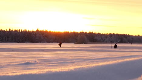 Slider-shot-of-men-ice-fishing,-on-snow-covered-ice,-at-sunset,-on-a-sunny,-winter-evening,-in-Ostrobothnia,-Finland