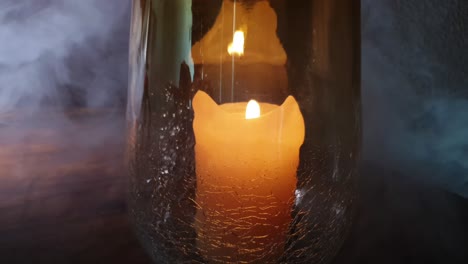 Haunted-and-spooky-orange-Candle-flame-burning-and-flickering-in-a-beautiful-cracked-glass-flower-vase-on-a-wooden-table