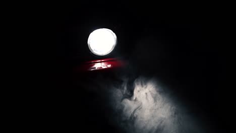 Fog-or-mist-moving-in-light-beam-of-red-car-round-headlight,-slow-motion-close-up