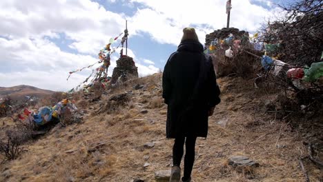 Behind-person-walking-up-hill-slow-motion-to-sacred-mountain-prayer-flags-blowing-in-wind-on-mountain-peak