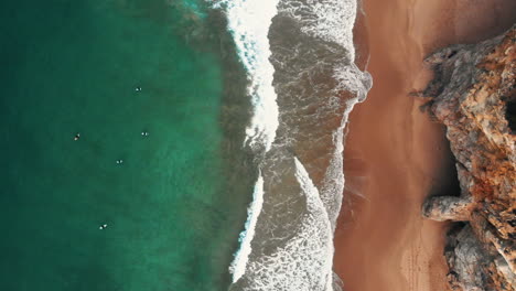aerial-shot-from-cliffs-to-the-ocean-with-surfers-waiting-for-a-waves