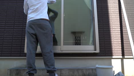 A-man-cleaning-the-exterior-of-a-glass-window-of-his-home---Mid-shot