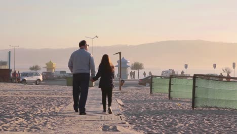 Rear-view-of-granddaughter-and-grandfather-walking-holding-hands-near-the-beach-at-sunset