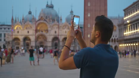 Young-man-taking-photos-on-his-phone-of-San-Marco-plaza-at-dusk-time