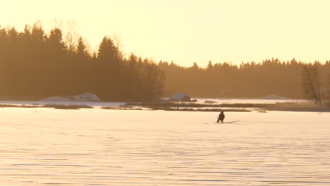 Silhouette-of-lonely-ice-fishing-man-on-frozen-lake-in-winter