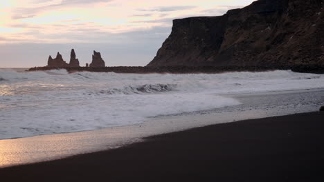 Basalt-cliffs-frame-powerful-waves-crashing-over-a-black-sand-beach-in-Vik-Iceland-at-sunset