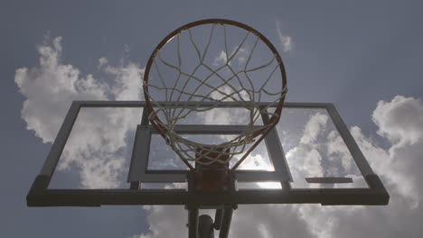 basketball-makes-a-basket-at-an-outside-court,-low-angle-camera-with-a-sun-flare