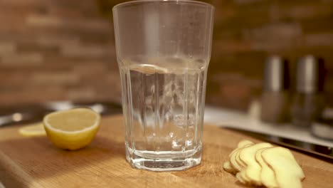 Heißes-Wasser-Aus-Dem-Wasserkocher-In-Das-Glas-Gießen,-Das-Neben-Geschnittenem-Ingwer-Und-Zitrone-Steht,-Still,-4k