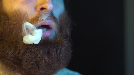 Extreme-Close-Up-bearded-Man-smoking-a-vaporizer-device-isolated-in-dimly-lit-area-in-slow-motion