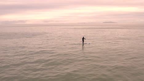 Paddle-boarder-riding-alone-on-calm-glowing-orange-seascape-horizon
