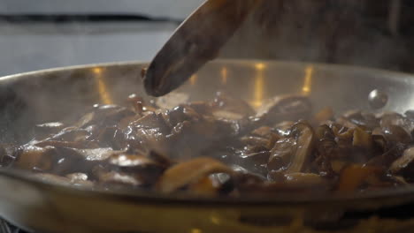 Stirring-mushrooms-with-wooden-spoon-with-moisture-evaporating,-slowmo
