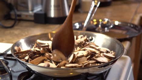 Mixing-raw-sliced-mushrooms-sizzling-in-frying-pan-with-wooden-spoon