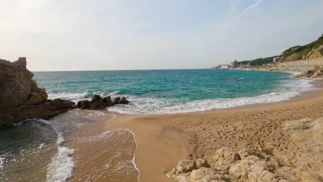 Hermosa-Playa-De-Arena-Mediterránea,-Maresme-Barcelona,-San-Pol-De-Mar,-Con-Rocas-Y-Mar-Tranquilo-Y-Turquesa