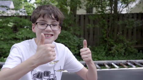 Cute-boy-sitting-on-trampoline-smiles-and-gives-camera-thumbs-up