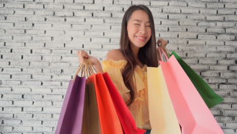 Slowmotion-shot-of-a-excited-young-woman-holding-colourful-shopping-paper-bags-and-smiling-to-the-camera