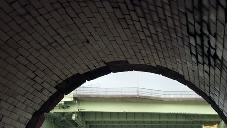 Under-brickwork-tiled-stone-industrial-archway-view-of-arched-steel-girder-railway-bridge-crossing