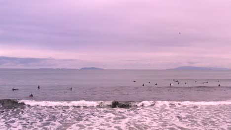 Aerial-push-in-over-gathering-of-surfers-on-Ventura-beach-ocean-waves