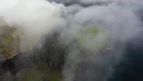 Rugged-Faroe-Islands-coastline-through-sea-clouds,-high-aerial-birds-eye-view