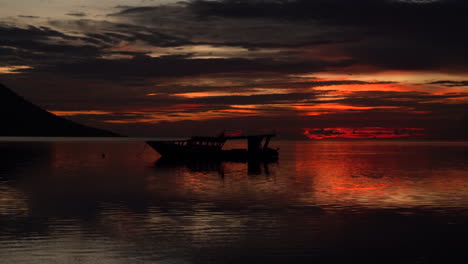 A-silhouette-of-a-volcano-and-small-boat-during-a-fiery-sky-sunset-as-the-camera-zooms-in-to-focus-on-the-boat