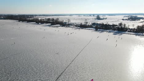 Aerial-shot-of-people-ice-skating-on-snowy-lake-after-frosty-night---Beautiful-sunlight-reflection-on-white-surface-in-Netherlands,Europe