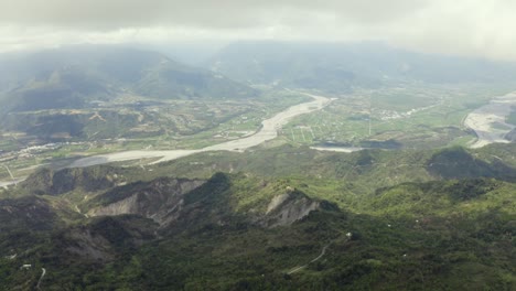 High-altitude-aerial-view-above-Dulan-mountains-through-clouds-to-vast-cultivated-farmland-,-Taitung-valley