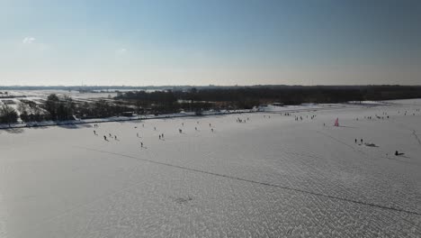 Aerial-shot-of-beautiful-snowy-landscape-with-playing-people-on-frozen-lake-during-sunlight-in-Netherlands