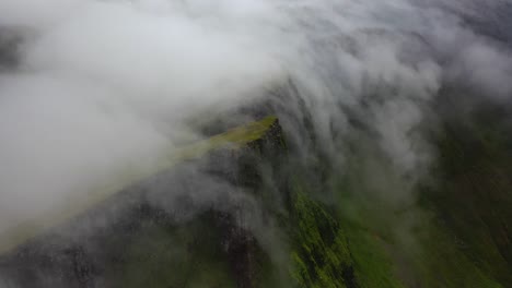 Clouds-rolling-over-steep-Faroe-Islands-hilltops-on-overcast-day,-aerial-view