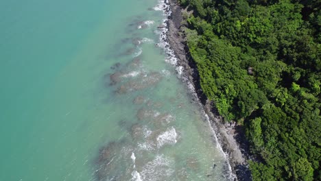 Salpicaduras-De-Olas-En-El-Arrecife-Del-Océano-En-Cape-Tribulation-Con-La-Selva-Tropical-De-Daintree,-Queensland,-Australia