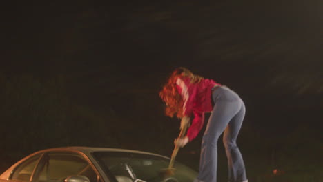 A-red-haired-woman-smashes-a-pizza-paddle-on-a-car-windshield
