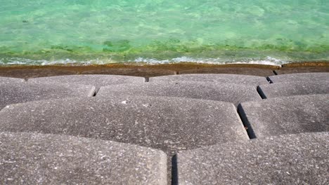 gentle-turquoise-waves-brakes-on-concrete-shore,-slow-motion