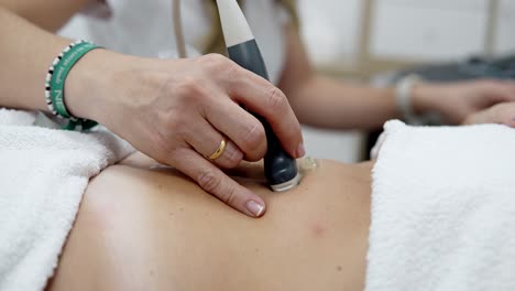 Female-Doctor-Moving-Ultrasound-Machine-On-Patient's-Body-In-Clinic