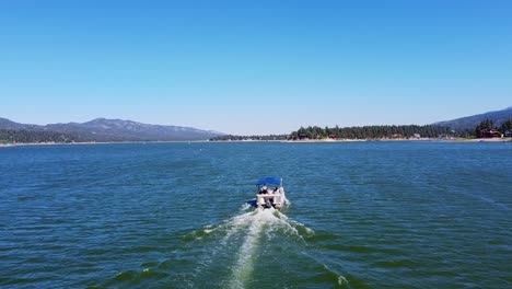 Aerial-view-following-rental-boat-on-Big-Bear-Lake-in-the-San-Bernardino-National-Forest-of-California-with-blue-sky-and-mountains-in-the-background
