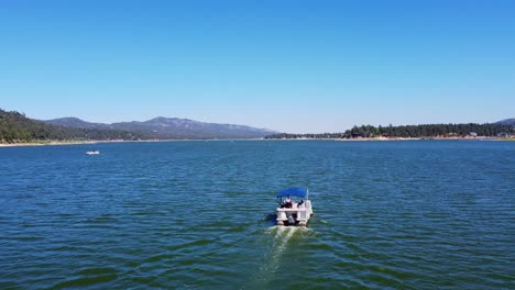 Aerial-reveal-of-rental-boat-on-Big-Bear-Lake-in-the-San-Bernardino-National-Forest-of-California-with-blue-sky-and-mountains-in-the-background
