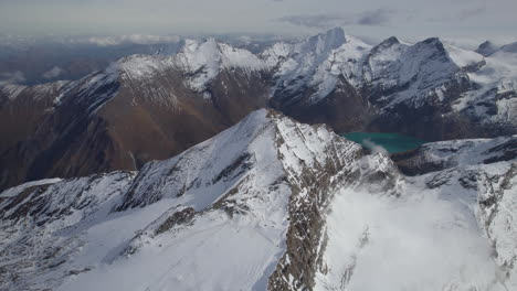Drohnenaufnahme-Eines-Grünen-Bergsees,-Umgeben-Von-Schneebedeckten-Alpen-In-Österreich