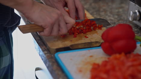 Closeup-of-man-hand-with-knife-cutting-fresh-red-pepper-on-wooden-board