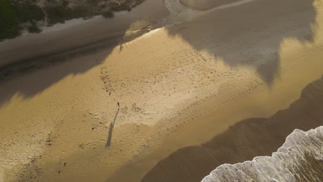 Luftaufnahmen-Von-Oben-Nach-Unten-Von-Jungen-Surfern,-Die-Aus-Dem-Wasser-Kommen-Und-Bei-Sonnenuntergang-Am-Sandstrand-Spazieren-Gehen