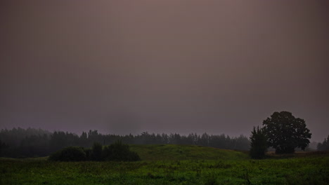 Gray,-foggy-morning-turns-golden-as-the-sunrise-illuminates-the-sky-above-lush,-green-countryside---time-lapse