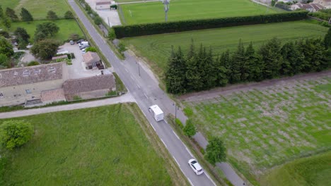 Aerial-tracking-shot-of-a-white-delivery-truck-driving-through-the-countryside
