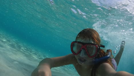 Selfie-Subacuático-De-Una-Niña-Pelirroja-Con-Máscara-De-Buceo-Y-Snorkel-Levantando-Arena-Con-La-Mano-Del-Fondo-Del-Mar-Y-Nadando-En-Agua-Clara-Del-Océano