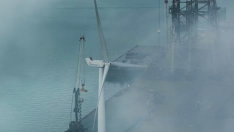 Luftdrohne-Durch-Den-Nebel-Einer-Windkraftanlage,-Die-Sich-Langsam-An-Einem-Hafen-Dreht
