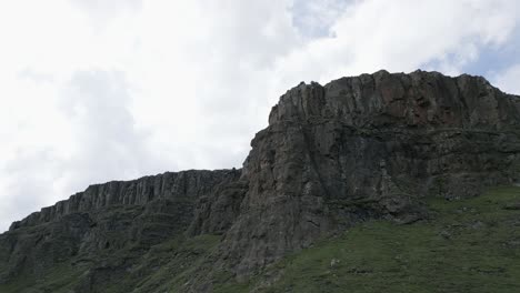 Aerial-flight-toward-steep-rocky-cliffs-off-green-mountain-plateau