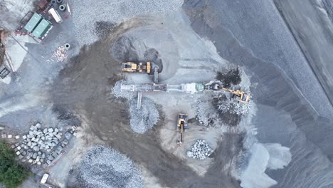 Drone-shot-of-bob-cat-and-mining-excavator-moving-rocks,-with-conveyor-belt-sorting-rocks-with-rubble-into-piles-in-quarry-mine
