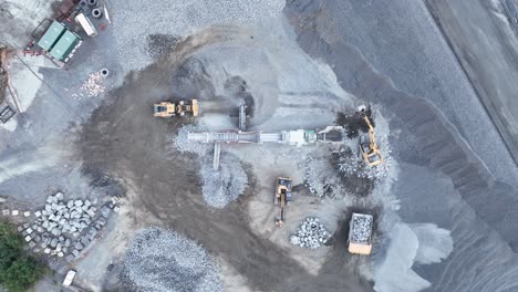 Drone-shot-of-bob-cat,-dump-truck-and-mining-excavator-moving-rocks,-with-conveyor-belt-sorting-rocks-with-rubble-into-piles-in-quarry-mine