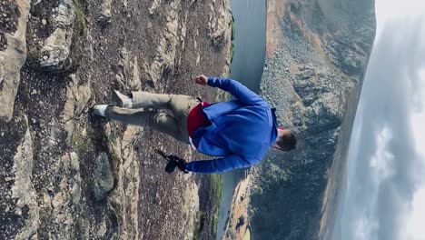 Man-holding-camera-walks-to-cliff-overlooking-Guinness-Lake-Ireland