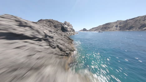 FPV-drone-flying-low-above-Mediterranean-rocky-coast-and-turquoise-clear-water