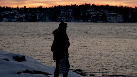 Silhouette-of-a-woman-walking-by-the-water,-a-lake-in-winter-with-snow