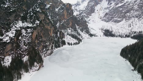 Vista-Aérea-Sobre-El-Lago-Braies-Congelado-Con-Montañas-Cubiertas-De-Nieve-En-El-Fondo-En-Trentino,-Italia---Disparo-De-Drones