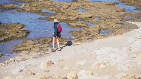 A-young-woman-walks-towards-the-sea-in-Shekmona,-Haifa,-Israel